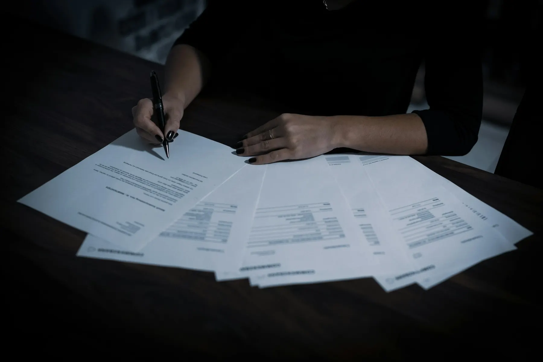 Une main signe un document posé parmi d’autres feuilles sur un bureau