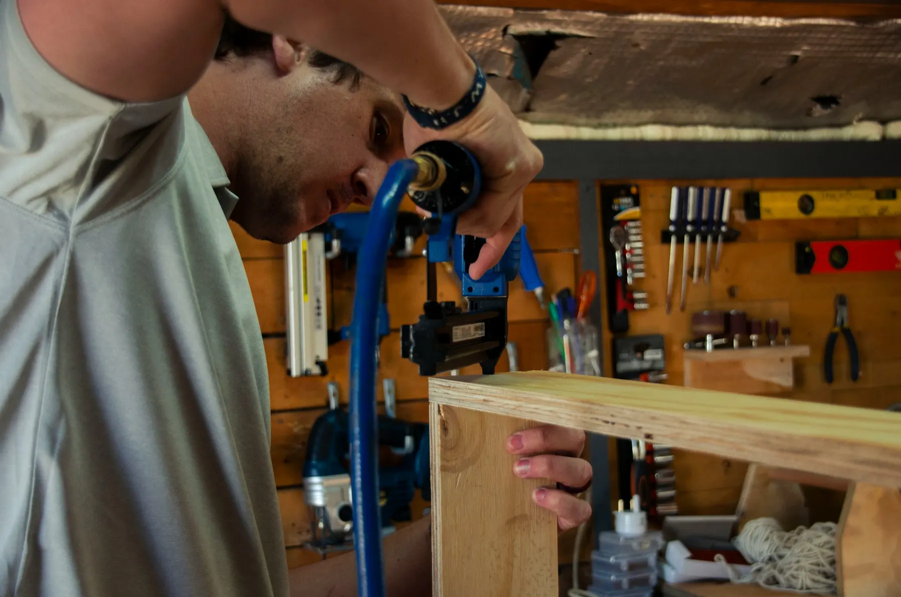 Un menuisier agrafe un cadre de contreplaqué dans son atelier, les outils accrochés au mur